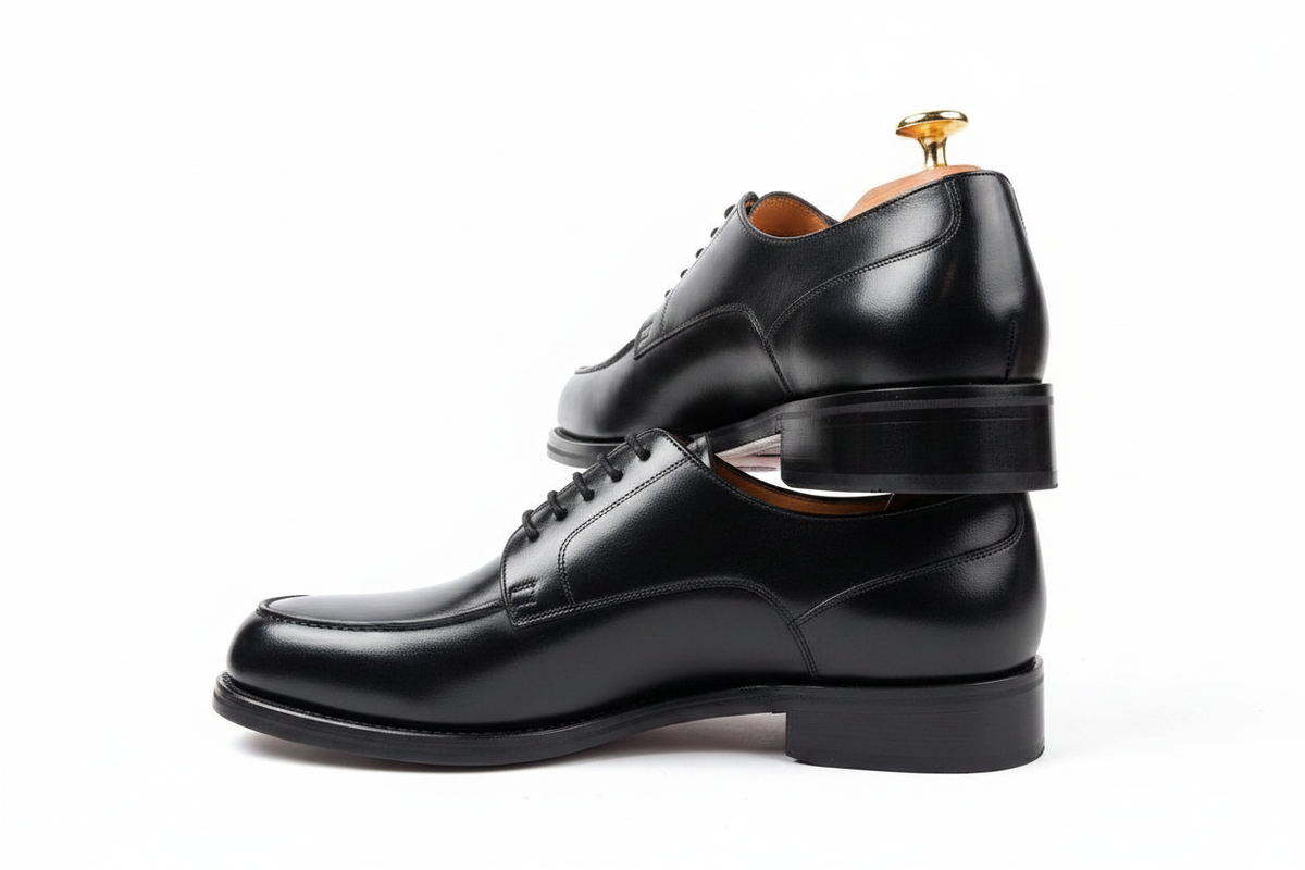 Derbies noirs en composition empilée avec embauchoir en bois doré sur fond blanc