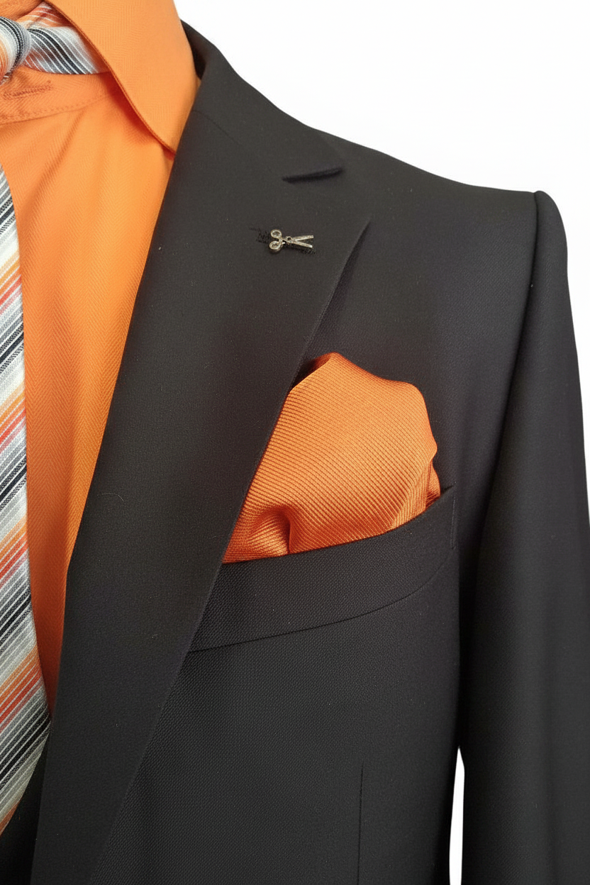 Gros plan revers noir avec pin libellule argenté, pochette orange et cravate rayée sur fond blanc