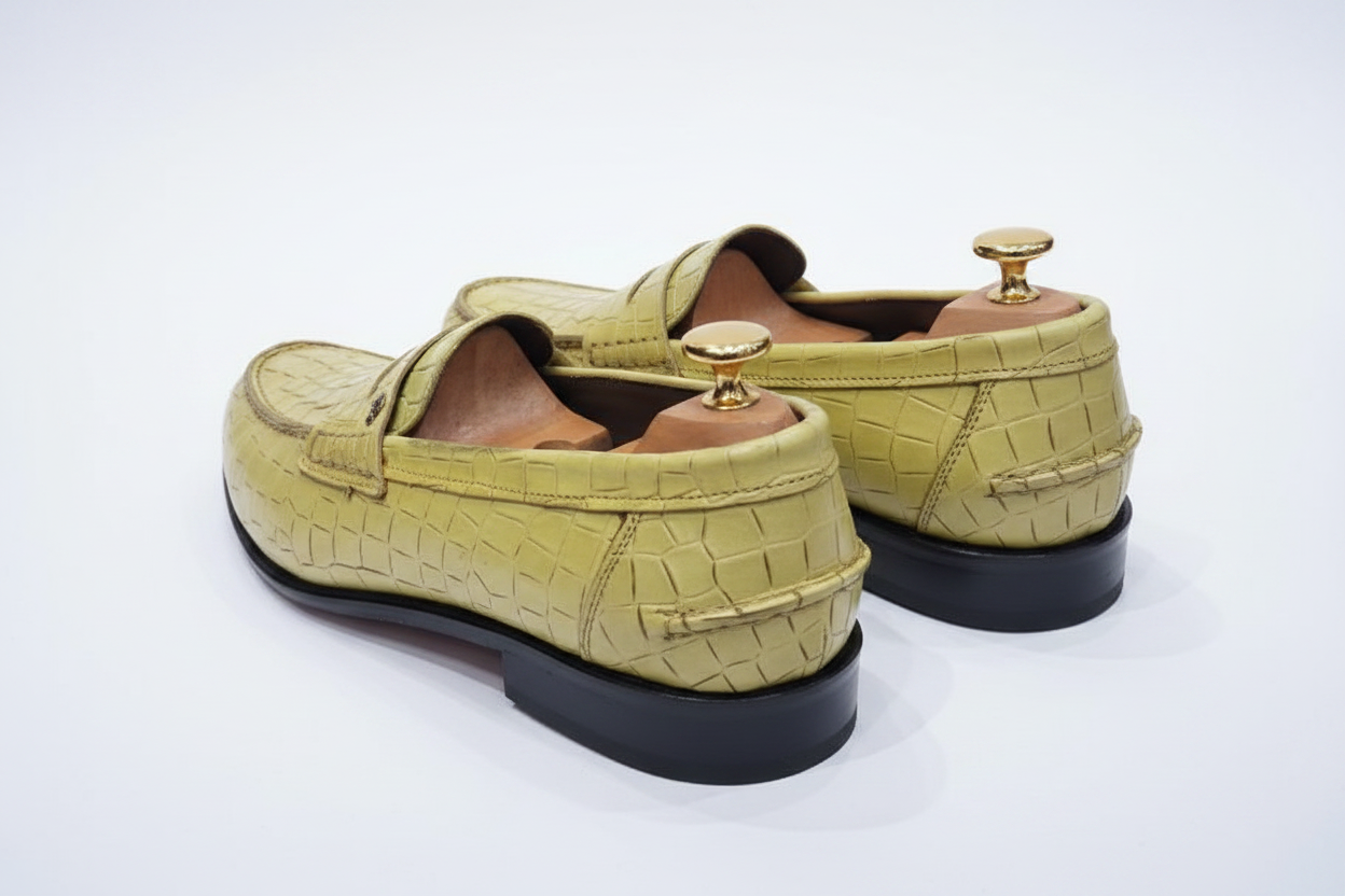 Mocassins penny loafer cuir croco embossé vert olive chartreuse vue trois-quarts arrière droite contrefort talon empilé noir intérieur caramel embauchoirs cèdre boutons dorés écailles croco flancs arrière fond blanc pur studio luxe