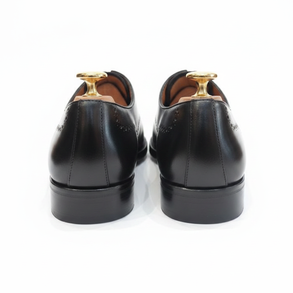 Oxford brogue noir vue arrière dos contrefort talon empilé cuir perforations brogue bord supérieur embauchoirs cèdre boutons dorés laiton grands ronds intérieur cuir caramel fond blanc pur studio luxe