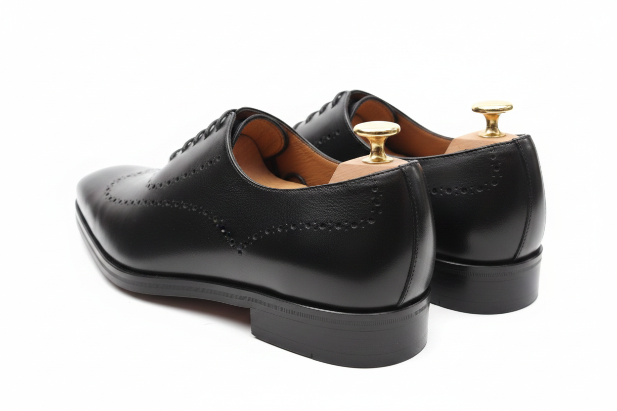 Oxford brogue noir vue trois-quarts arrière gauche deux chaussures décalées semelle cuir épaisse empilée contrefort embauchoirs cèdre boutons dorés tige intérieur caramel perforations brogue côté fond blanc pur studio luxe